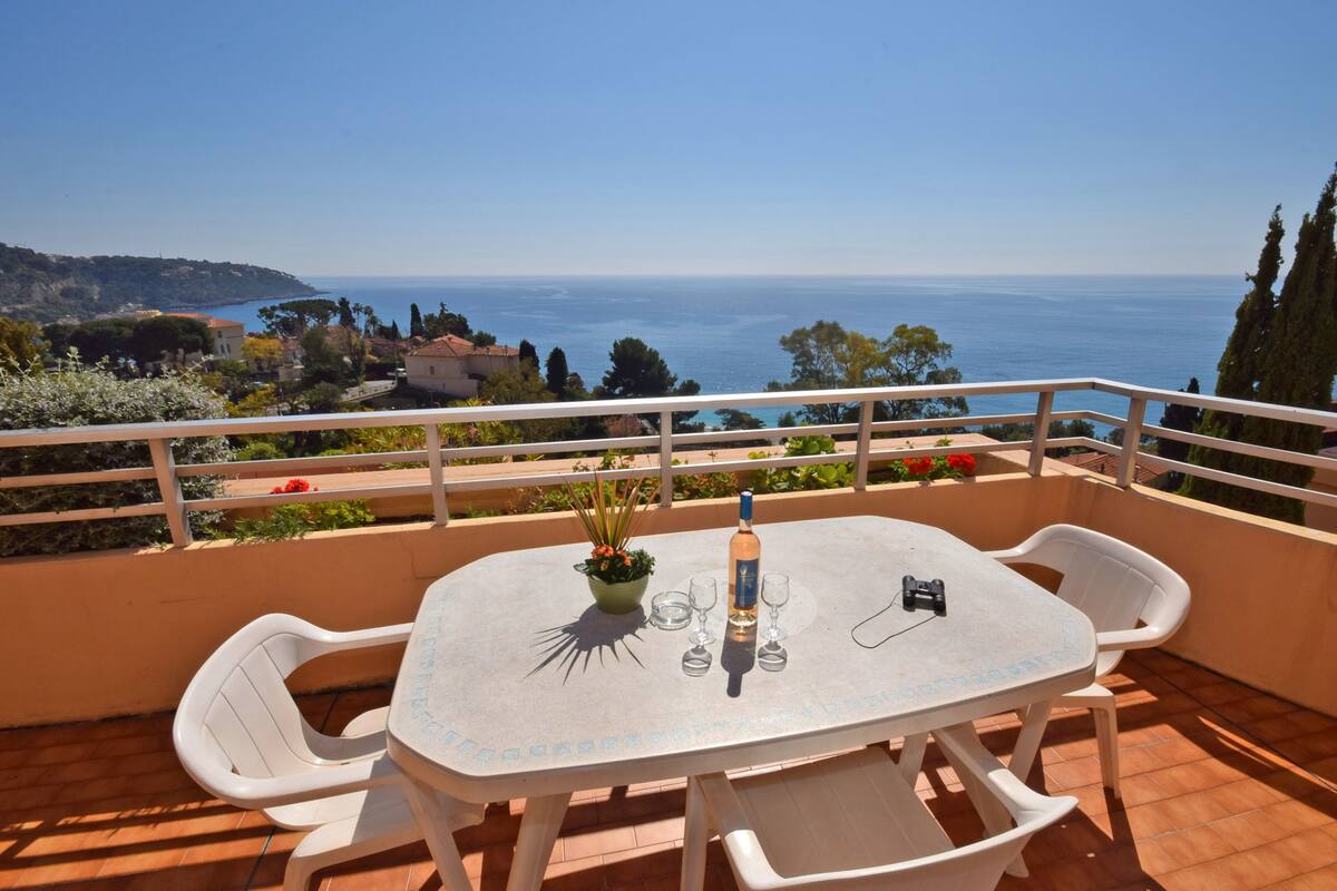 A terrace with a table and chairs, a bottle, and wine glasses.