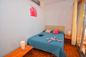 Quarto com cama, almofadas, mesa de cabeceira com abajur e janela com cortinas.
