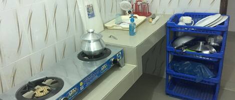 Een keukenhoek met een gasfornuis, een waterkoker en een blauwe plastic plank met servies.