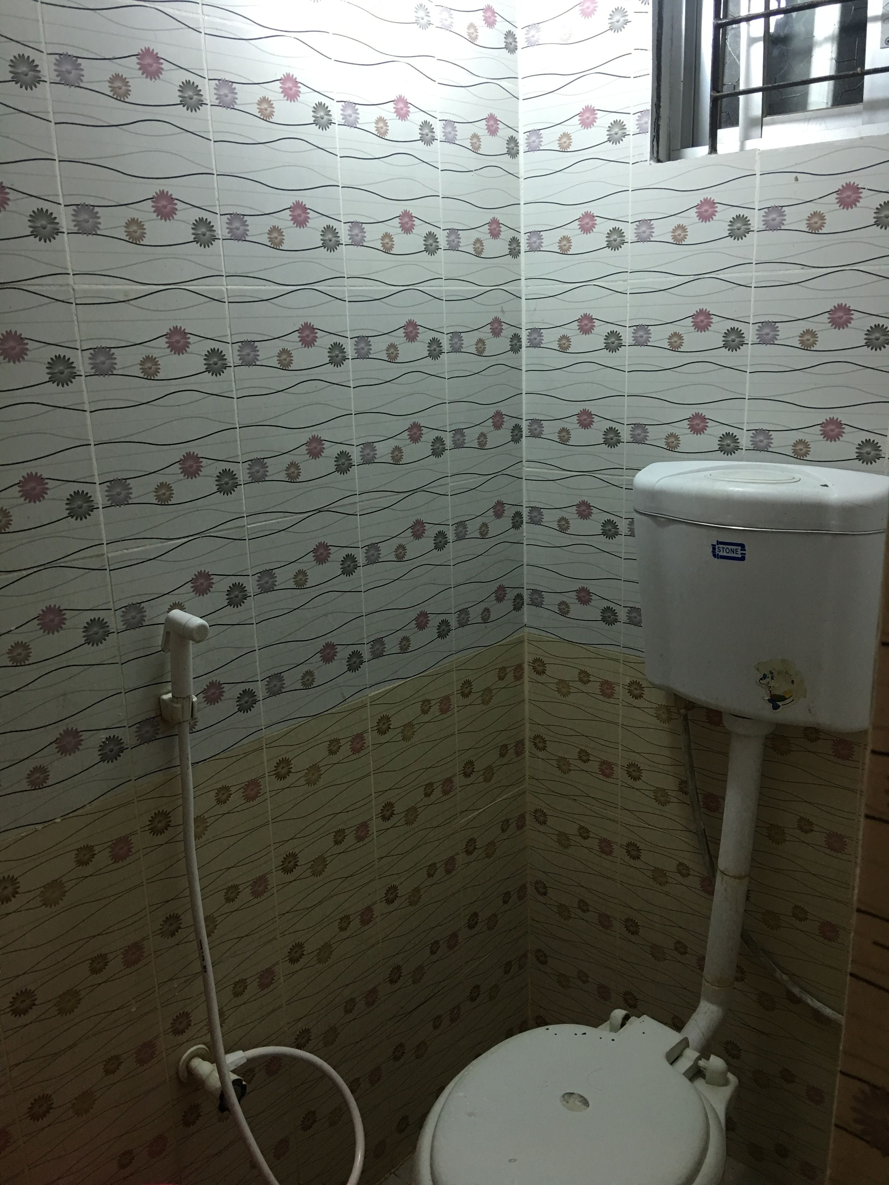 A small bathroom with a toilet, a shower, and a wall with a floral pattern.
