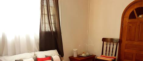 A neatly made bed with a red blanket, a bedside table with a lamp, and a wooden chair.