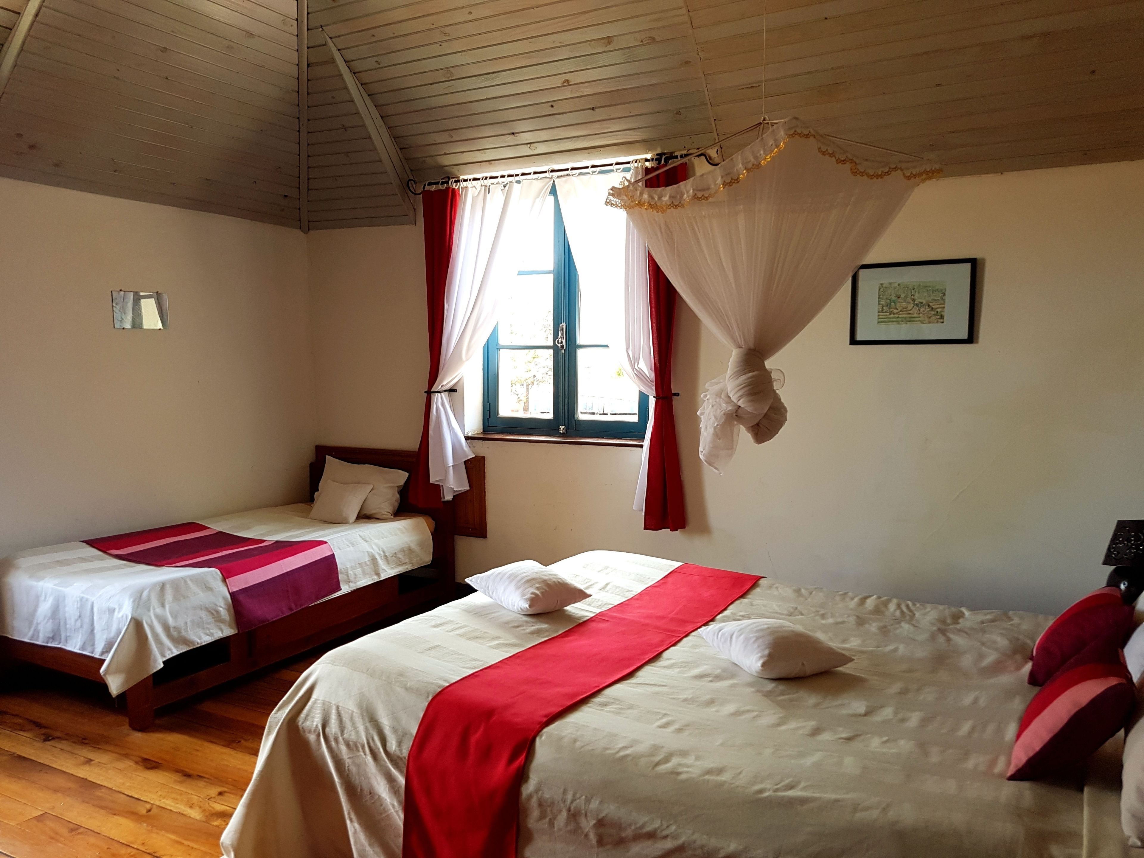 A room with two beds, a window with curtains, a ceiling fan, and a framed picture on the wall.
