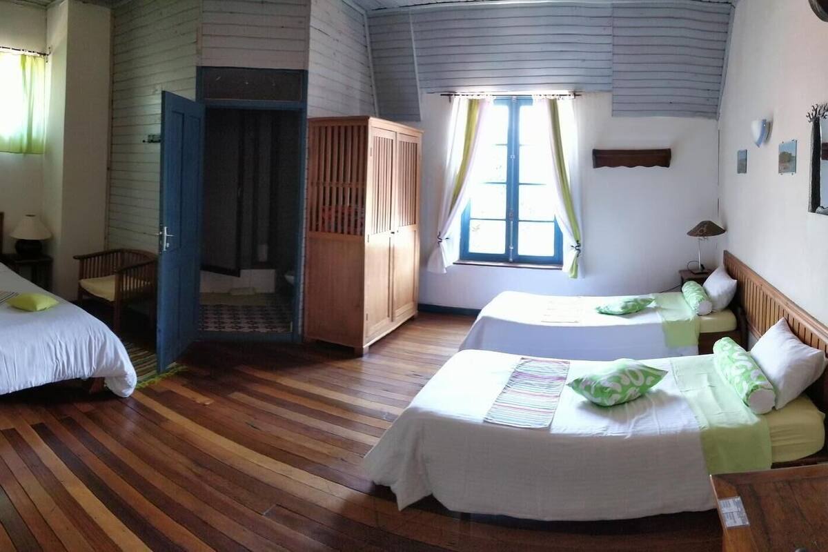 A room with two beds, wooden flooring, a small table, and a door leading to another room.