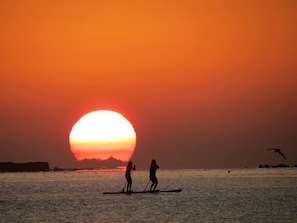 Ein Sonnenuntergang über einem Gewässer, während zwei Personen auf Paddleboards fahren.