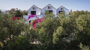 A white building with multiple windows and balconies, surrounded by dense greenery and pink flowers. - Orionas Village (Chania)