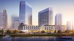 A modern high-rise building with a unique geometric facade, situated next to a body of water with a Ferris wheel in the background. - InterContinental Quanzhou by IHG (Quanzhou)