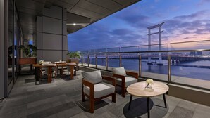 A modern outdoor seating area with a view of a bridge and river at dusk. - InterContinental Quanzhou by IHG (Quanzhou)