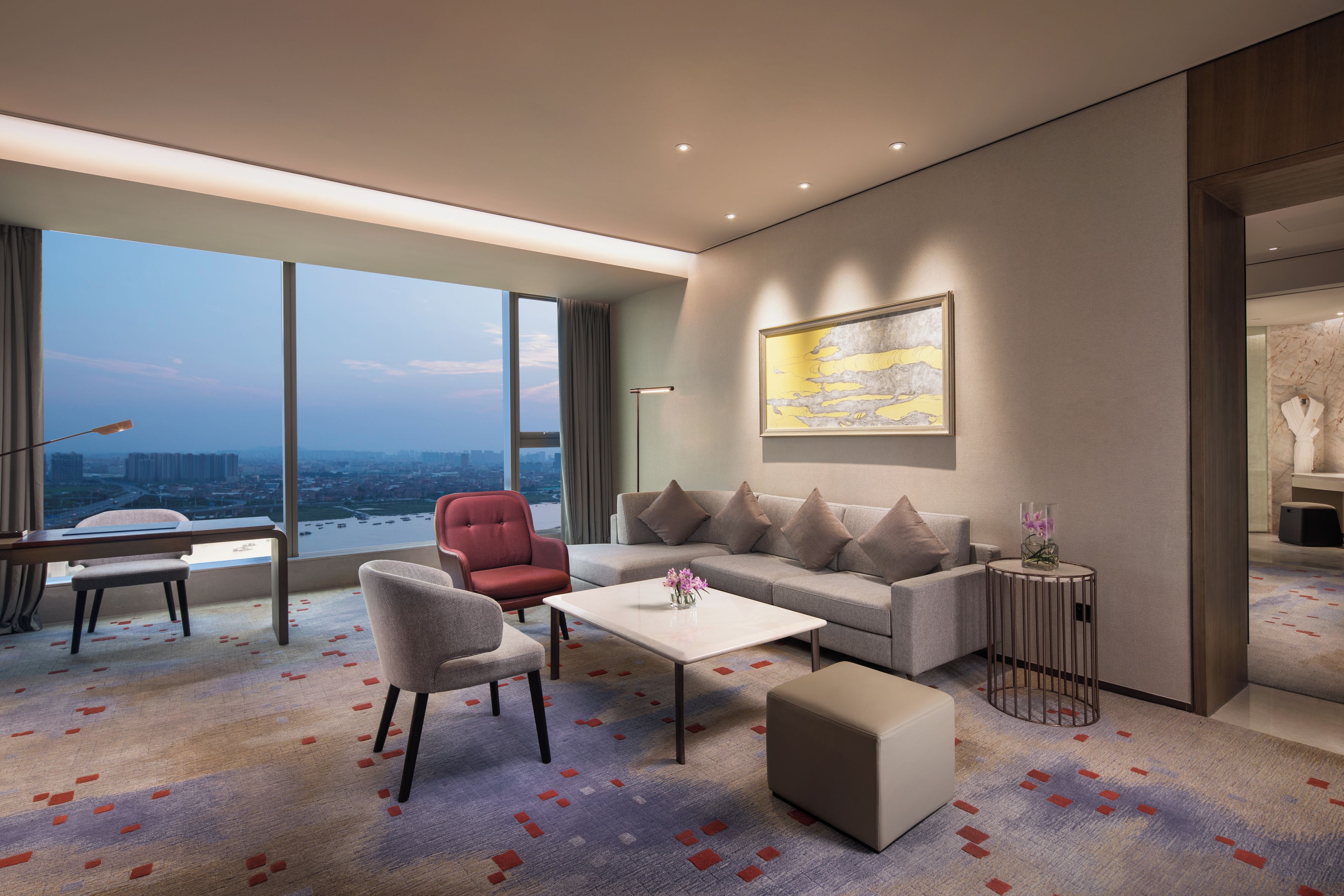 A modern living room with a sofa, armchairs, a coffee table, and a view of a cityscape through large windows.