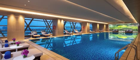 Una piscina interior moderna con zonas de descanso, ventanas amplias y vistas a la ciudad.