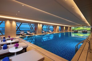 Una piscina interior moderna con zonas de descanso, ventanas amplias y vistas a la ciudad.