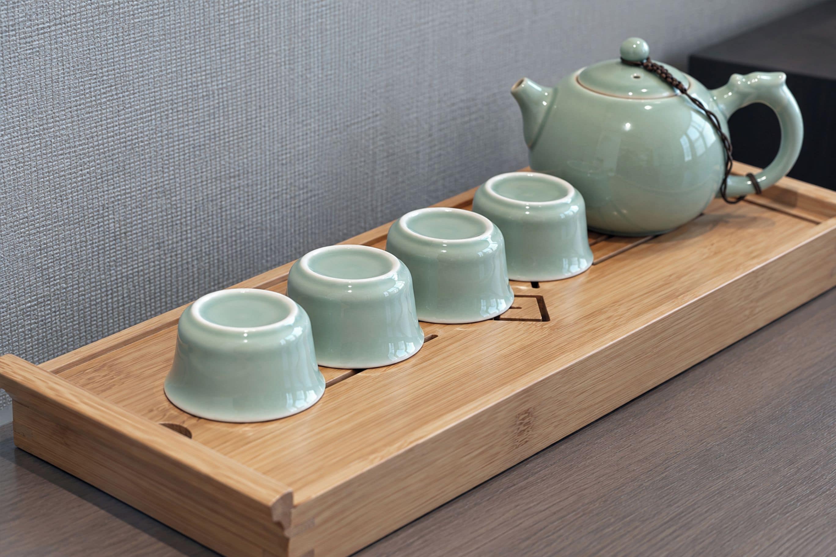 A tray with four ceramic cups and a teapot on a wooden tray.