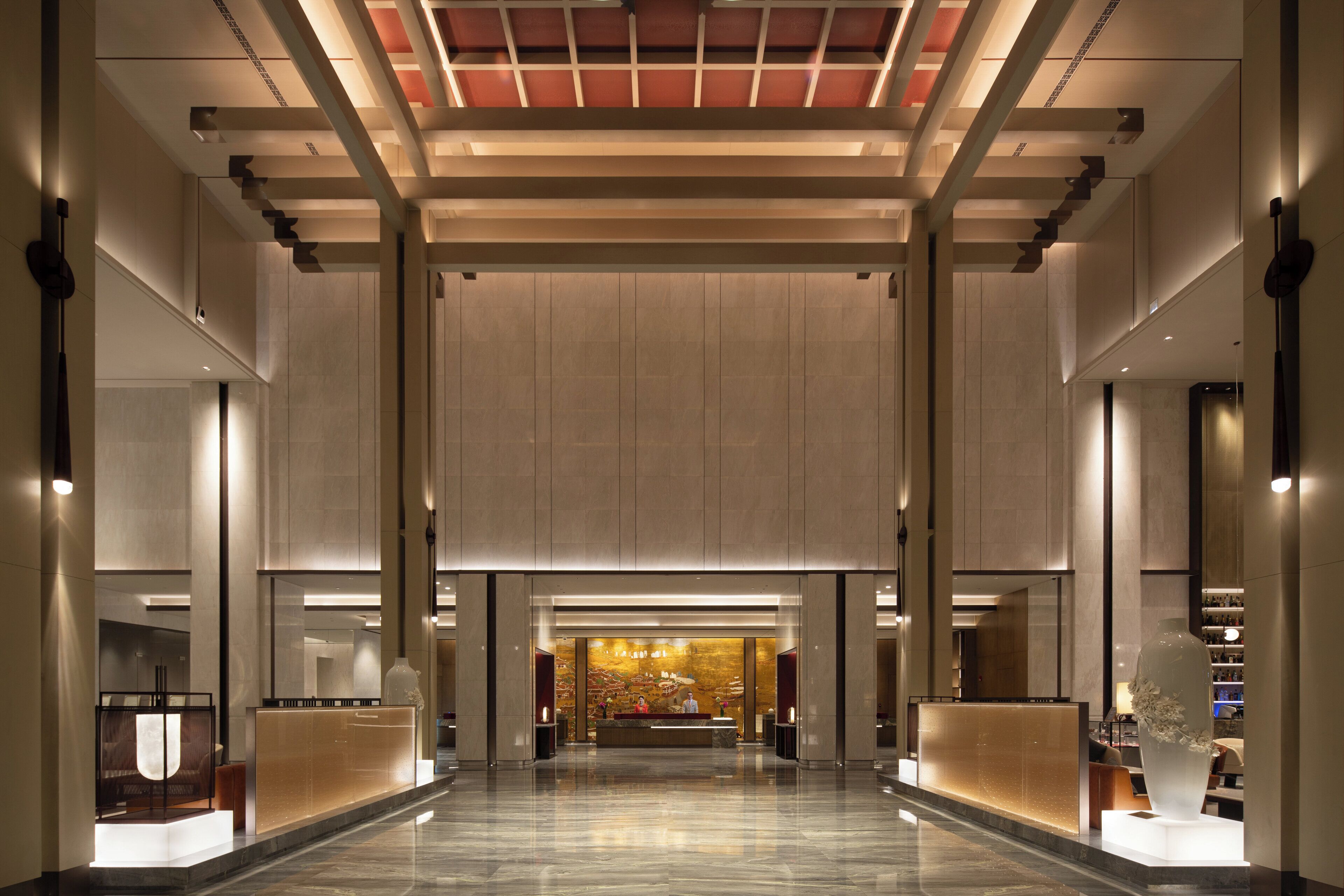 A spacious lobby with a reception desk, a large vase, and a modern ceiling design.