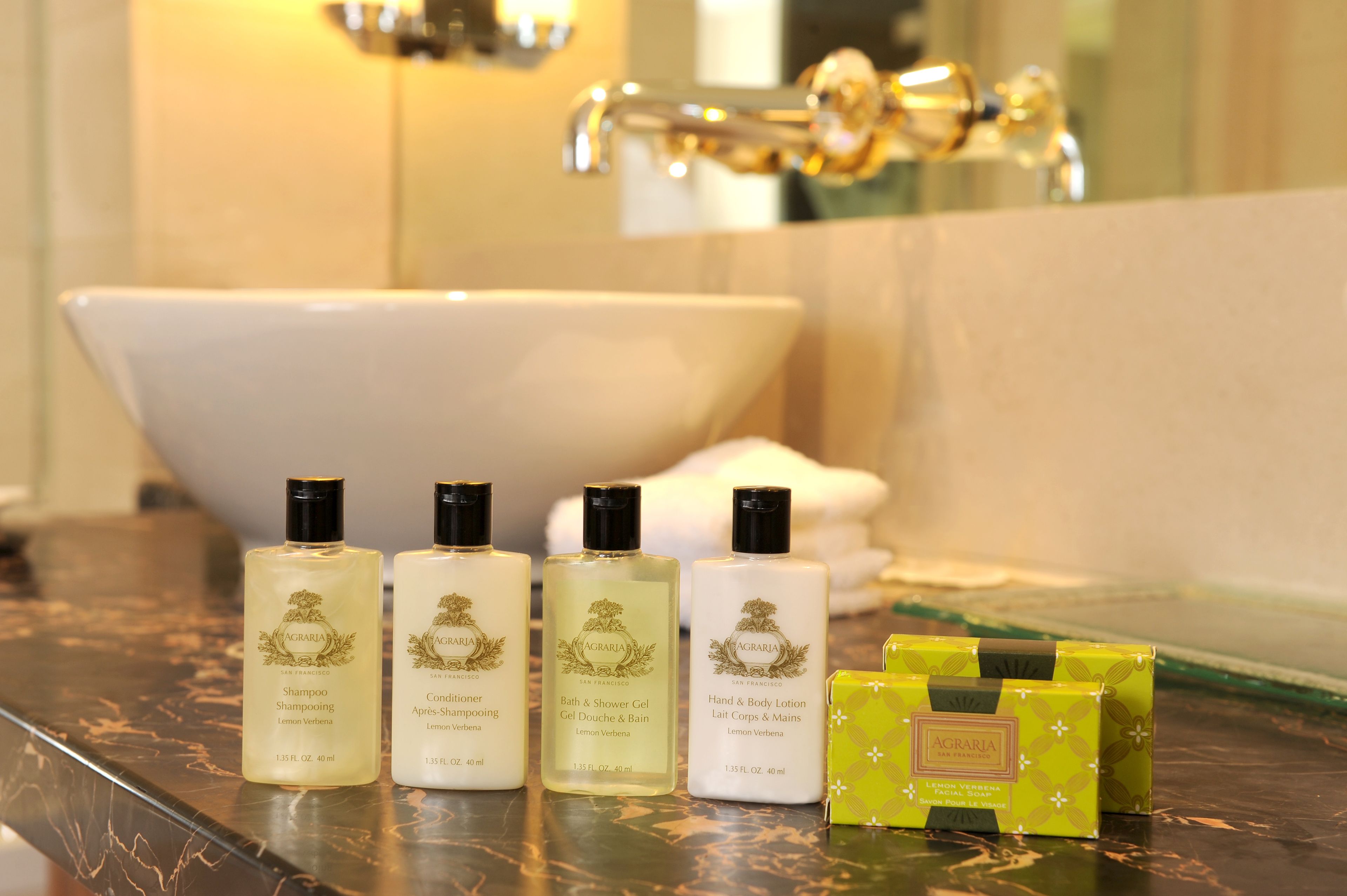 A bathroom with a bathtub, three bottles of AGRARIA products, and a green box on a marble countertop.