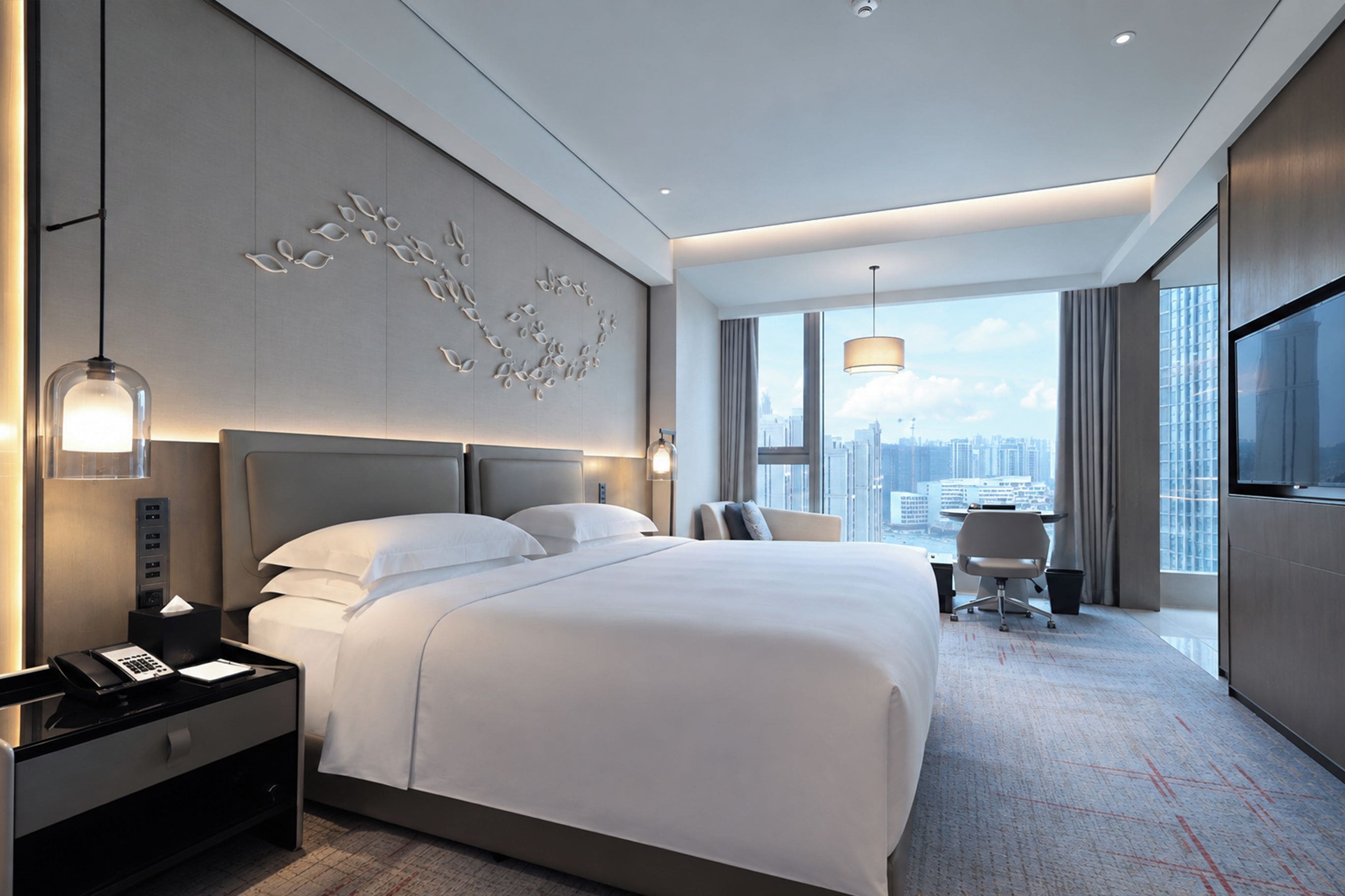 A modern hotel room with a large bed, a desk, and a city view.