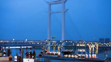 A bar setup with bottles and appetizers on a balcony overlooking a bridge.