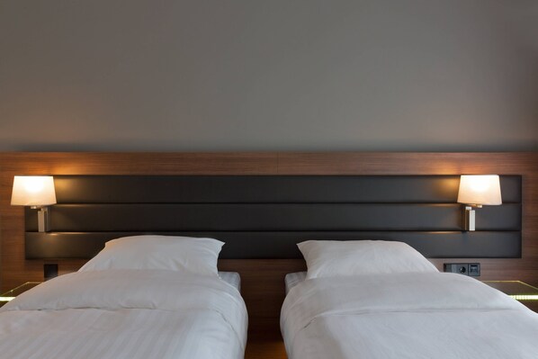 A hotel room with two beds, each with a headboard and bedside lamps.