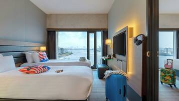 A hotel room with a large bed, a television, a desk with a lamp, and a view of the city and water.