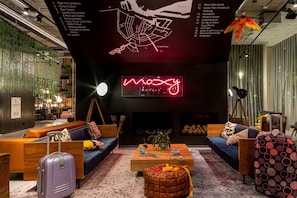 Um hall de hotel moderno com um letreiro de neon, áreas de estar e um mapa na parede.