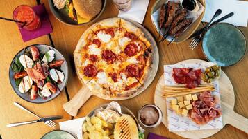 A variety of food items including pizza, salad, grilled meat, and chips on a wooden table.