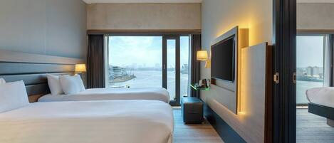 A hotel room with two beds, a TV, a desk, and a view of a cityscape.