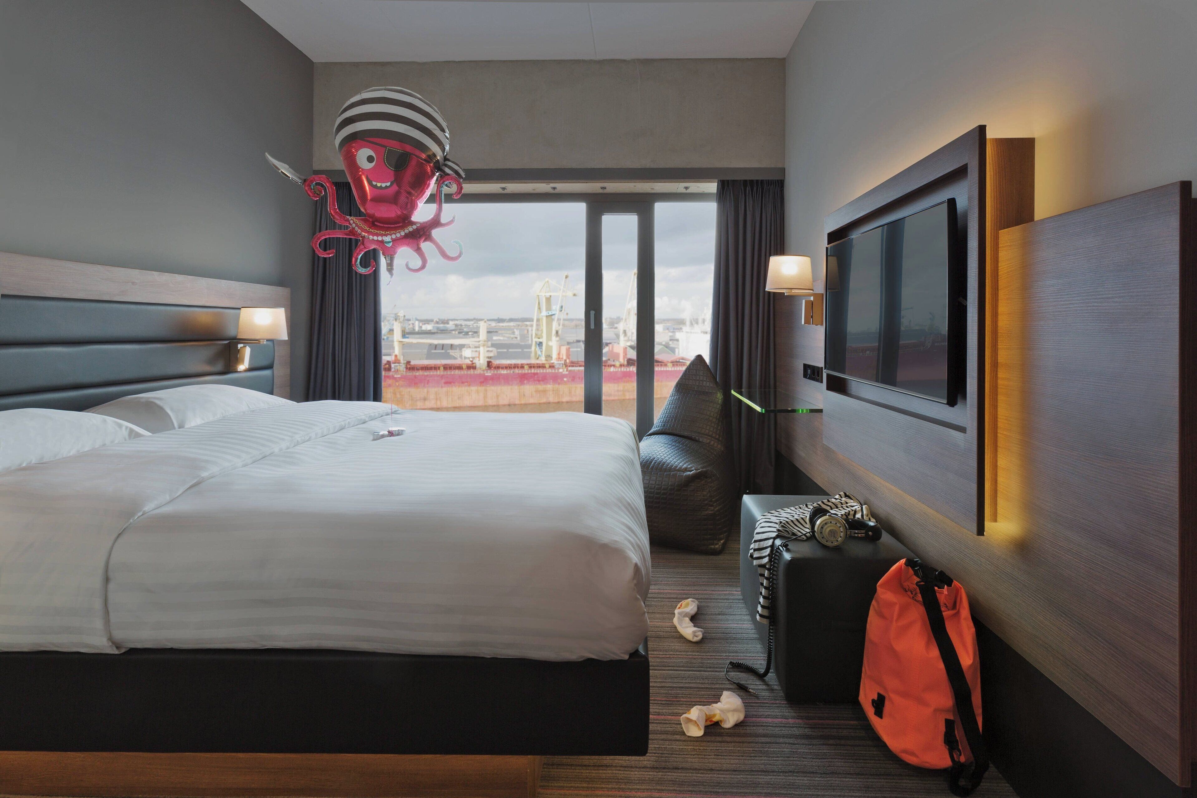 Hotelkamer met een groot bed, een televisie, een koffer en uitzicht op de stad.