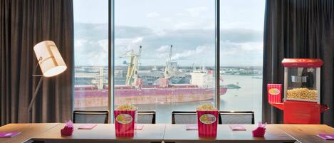 A dining area with a large window view of a port, a popcorn machine, and a table with chairs.
