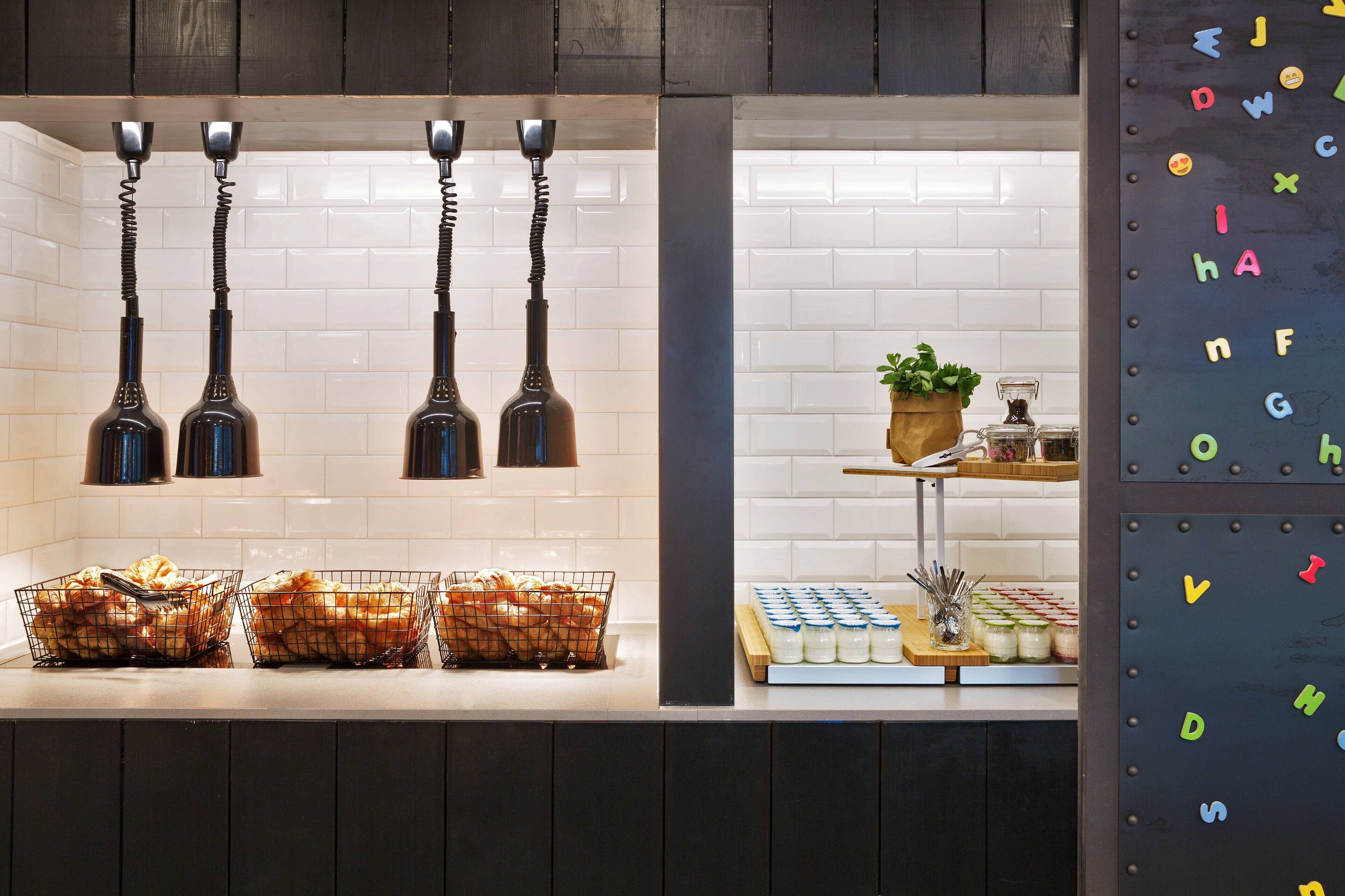 Una encimera de cocina con utensilios colgando, panes en cestas y una exposición de frascos.