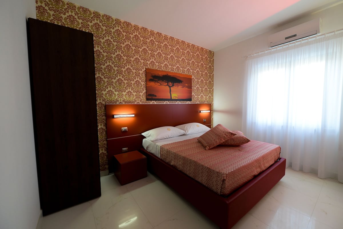 A bedroom with a bed, nightstands, a small table, a wall-mounted painting, and a window with curtains.