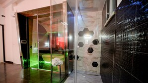 A modern elevator with glass doors, a marble wall with hexagonal patterns, and a black tiled wall. - X Hotel (Saviano)