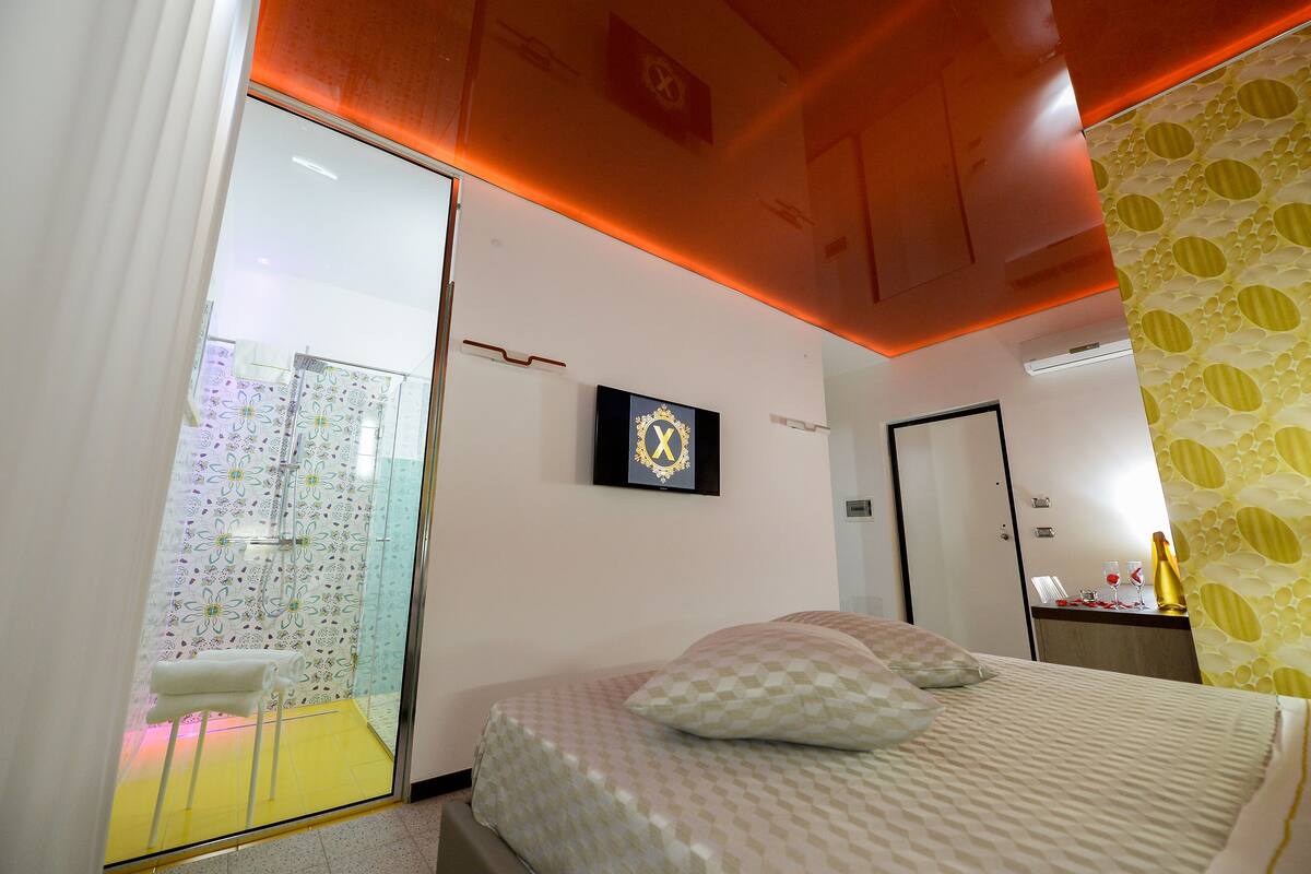 A hotel room with a bed, a shower area, and a small table with a lamp.