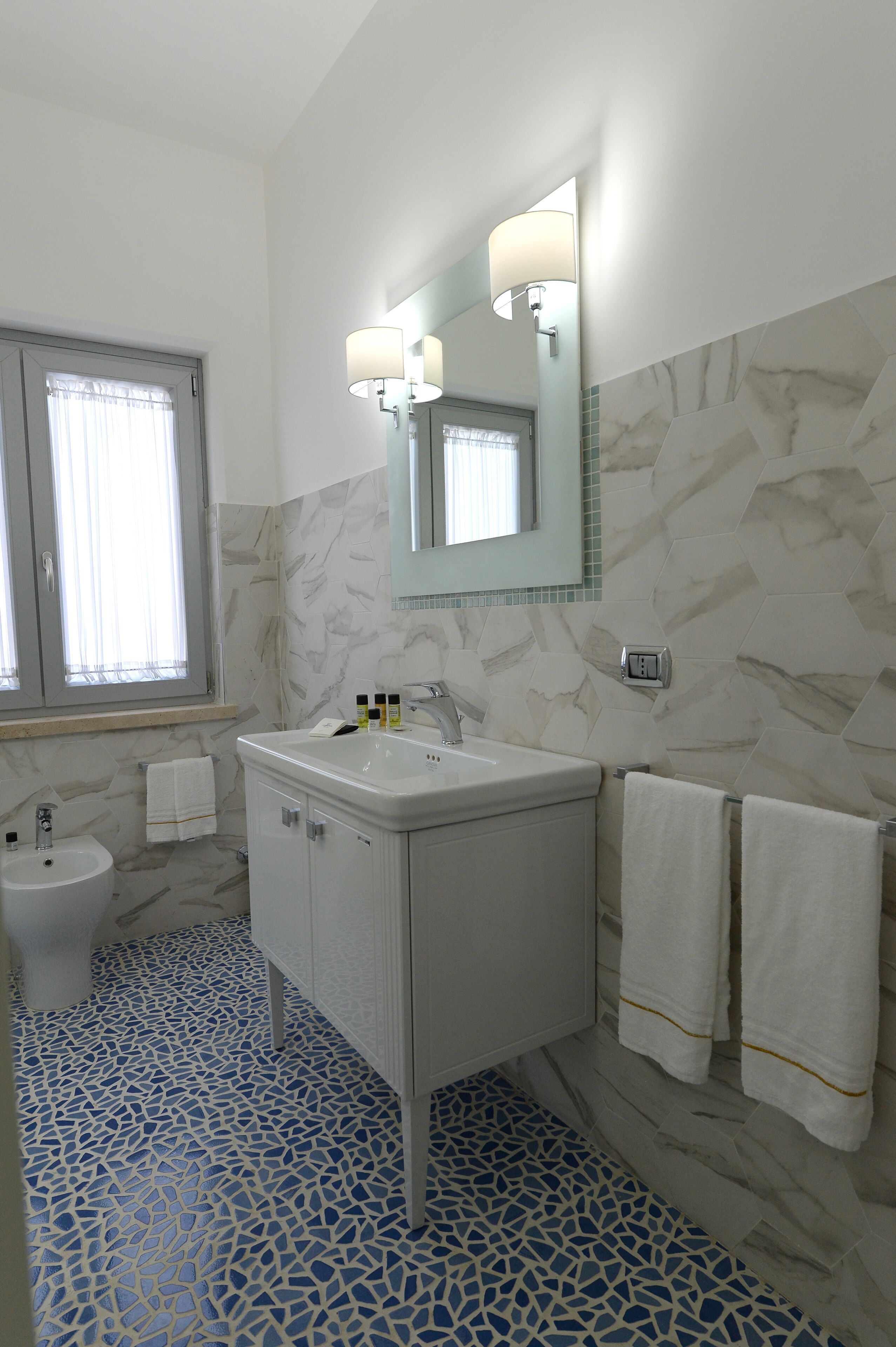 Een badkamer met een marmeren wand, een wastafel, een spiegel en een toilet.