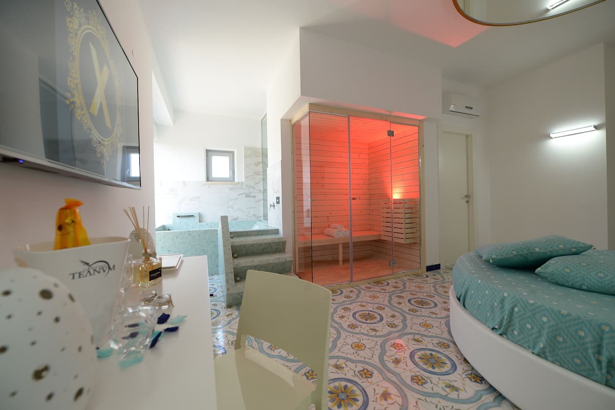 A bedroom with a bed, a chair, a table with a vase, and a mirror.