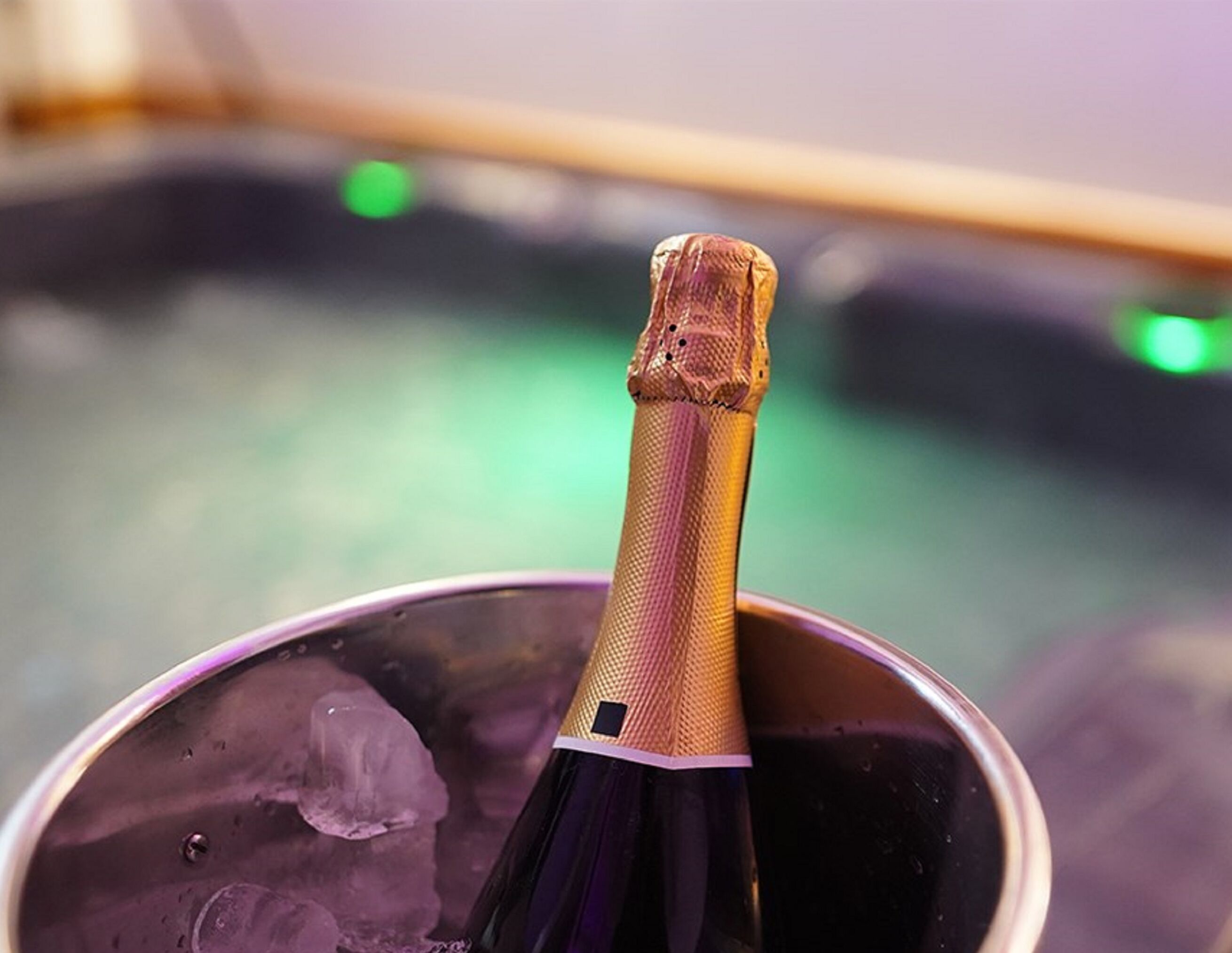 A bottle of champagne in a metal bucket with ice cubes.