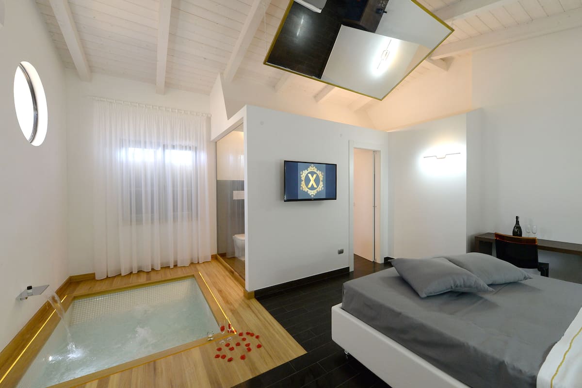 A modern bedroom with a bed, a small bathroom, a shower area, and a wall-mounted TV.