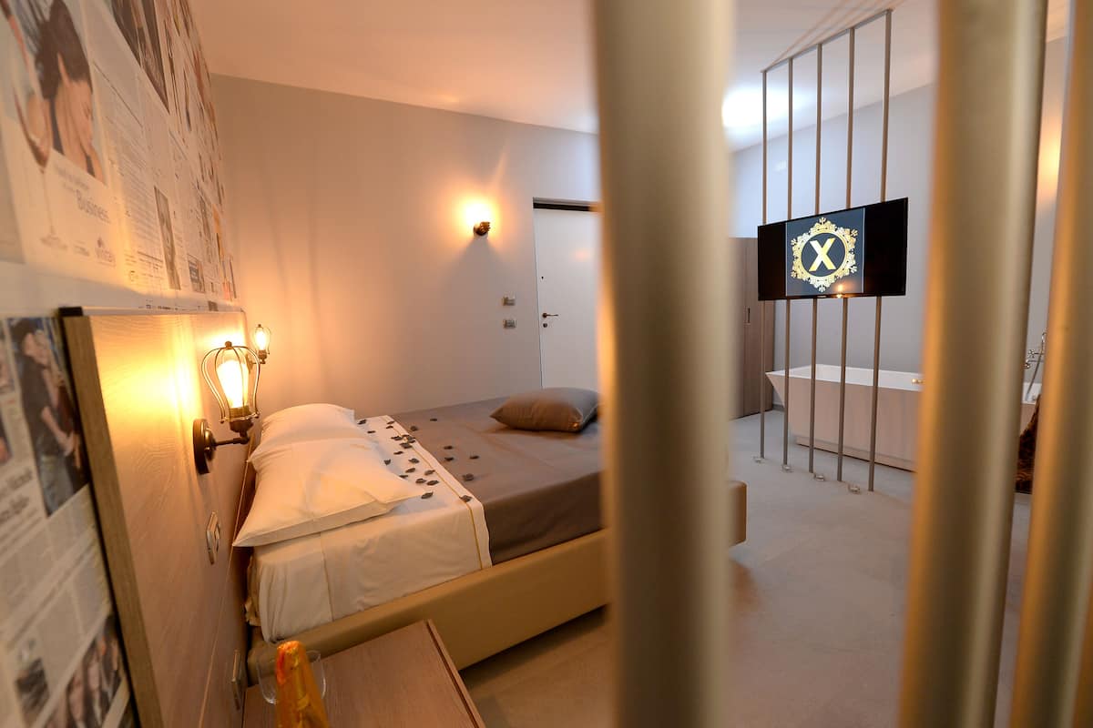 A hotel room with a bed, a wall-mounted TV, a bathroom with a bathtub, and a door with a lock.
