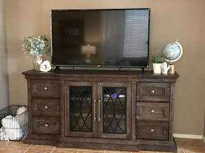 A dark wooden entertainment center with a flat-screen TV, glass-fronted cabinets, and decorative items including a globe and a cactus. - Ideal location for relaxation and adventure close to Phoenix  (Goodyear)
