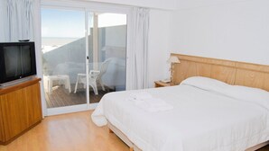 A hotel room with a bed, a TV, a small table, a chair, and a view of the beach through a sliding door. - Ivamar Hotel & Apart (Ostende)