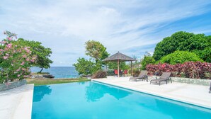 A pool area with a view of the sea, surrounded by greenery and a gazebo. - Luxury Oceanfront Villa w/Breathtaking Views! Infinity Edge Pool! (Llandovery, Laughlands)