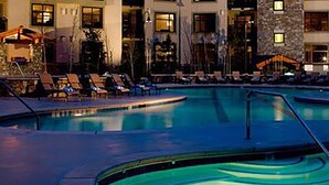 A swimming pool area with lounge chairs and a stone building in the background. - Monache, Mammoth Village, Luxury Studio (Mammoth Lakes)