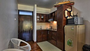 Une cuisine compacte avec des meubles en bois, un four à micro-ondes, un réfrigérateur et un petit coin repas avec des chaises blanches.