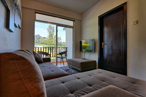A living room with a sofa, a television, and a sliding glass door leading to a balcony.