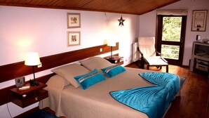 Un dormitori ben ordenat amb llit, taules de nit, una cadira, una làmpada penjant amb forma d'estrella, quadres a la paret i una finestra amb vistes.