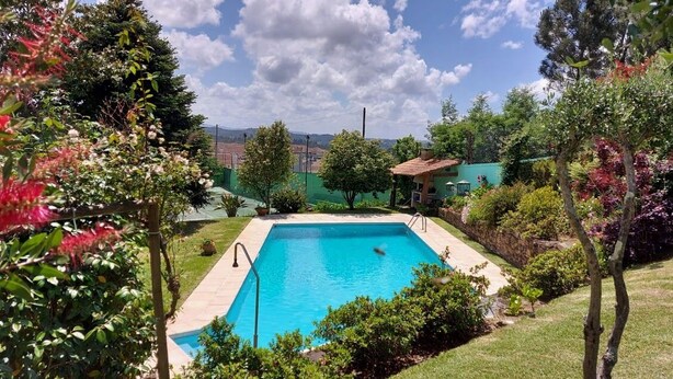 Una piscina rectangular envoltada de vegetació exuberant i un edifici petit amb teulada vermella.