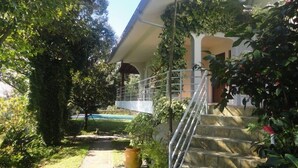Una casa amb un porxo cobert, escales de pedra i un camí de jardí que condueix a una piscina.