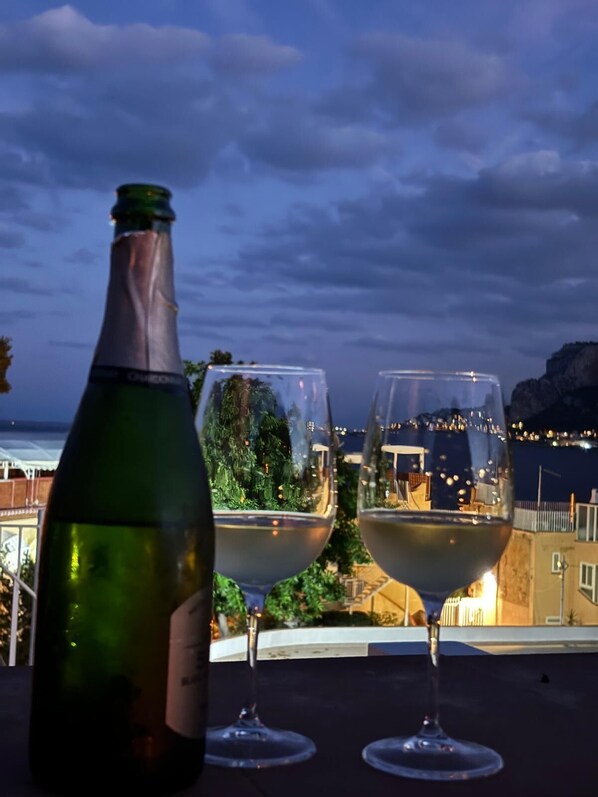 A bottle of wine and two wine glasses on a terrace with a view of the sea and buildings. - Athena apartments Mondello beach (Mondello)