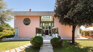 A modern two-story house with a central entrance, a circular window, and a well-maintained lawn. - A spacious, modern villa with a private pool (Cagliari)