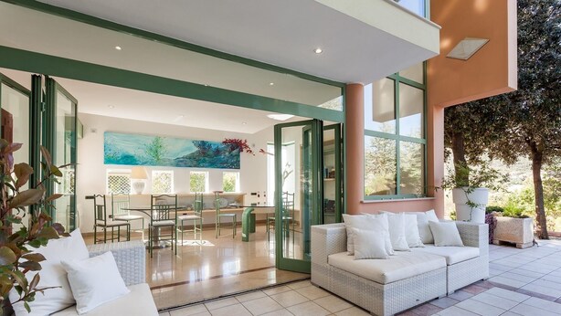 A spacious living area with a white sofa, a dining table with chairs, and a large window overlooking a garden. - A spacious, modern villa with a private pool (Cagliari)