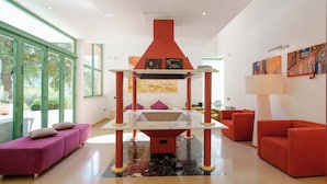 A modern living room with a central red and white structure, two red sofas, a purple sofa, and a large window with a view of greenery. - A spacious, modern villa with a private pool (Cagliari)