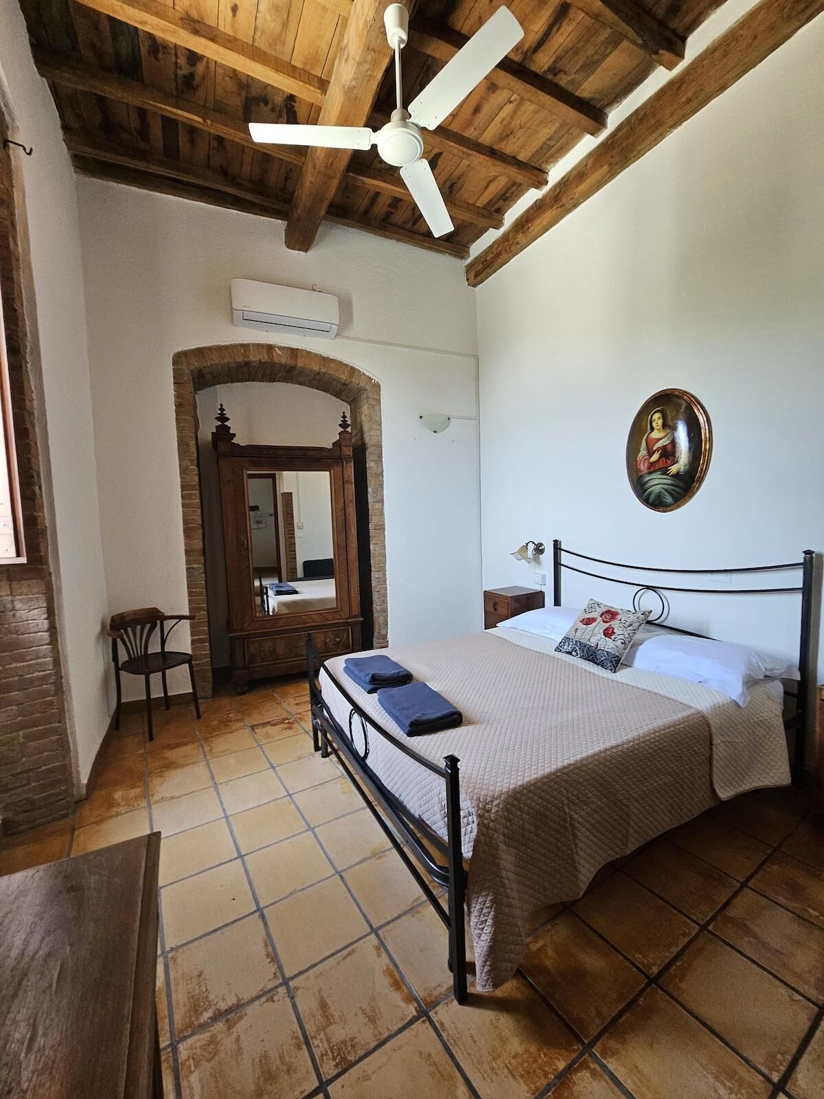 A bedroom with a bed, a ceiling fan, a mirror, and a door leading to another room.