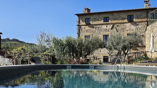 A pool with clear water reflecting the surrounding trees and a stone building with multiple windows in the background. - FARMHOUSE WITH PANORAMIC POOL IN PERUGIA/ASSISI IDEAL FOR GROUPS FOR 22 PLACES (Perugia)